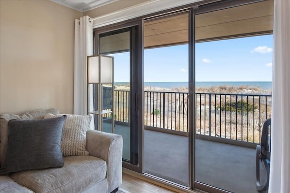 A room with a sofa, a large window, and a view of the beach.