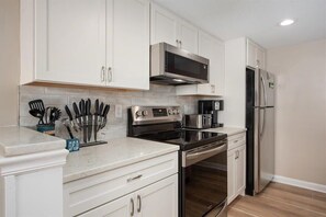 A kitchen with white cabinets, stainless steel appliances, and a marble countertop.