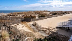 A beach with a wooden fence, a sandy area, and a white staircase leading down to the beach. - Completely Renovated Three Bedroom Oceanfront Condo (Ocean City)