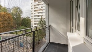 A balcony with a black metal railing, a white window, and a view of a multi-story building and trees. - Air-conditioned Studio with a Balcony | Close to Pola Mokotowskie (Warszawa)