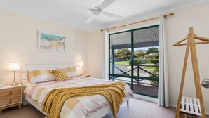 Un dormitorio con cama, lámparas de noche, ventilador de techo, ventana con vista al exterior y una escalera de madera.