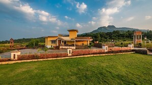 A large, yellow house with a spacious front yard and a mountain in the background.