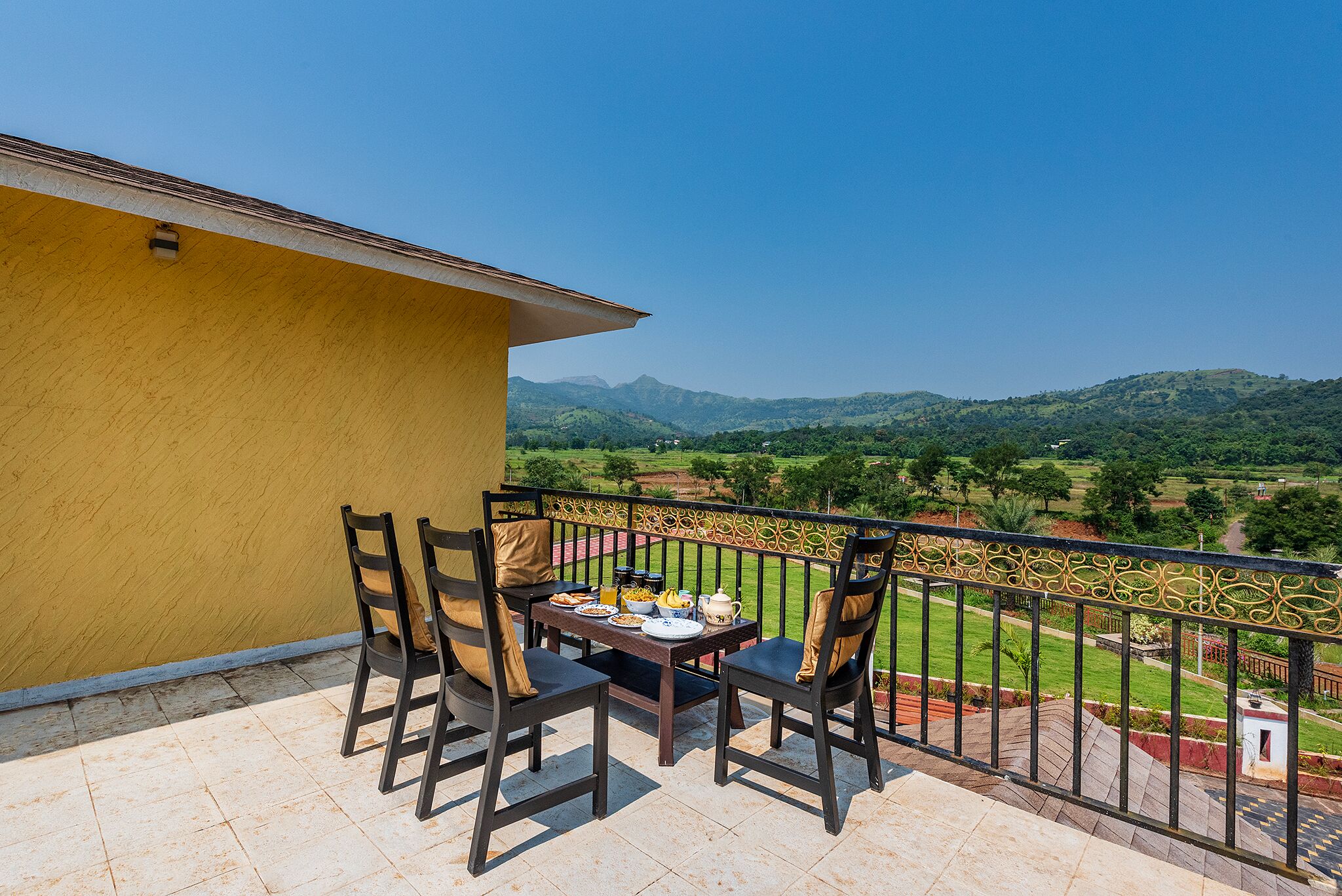 Un balcone con un tavolo apparecchiato per la colazione, affacciato su un paesaggio panoramico con colline e cielo sereno.