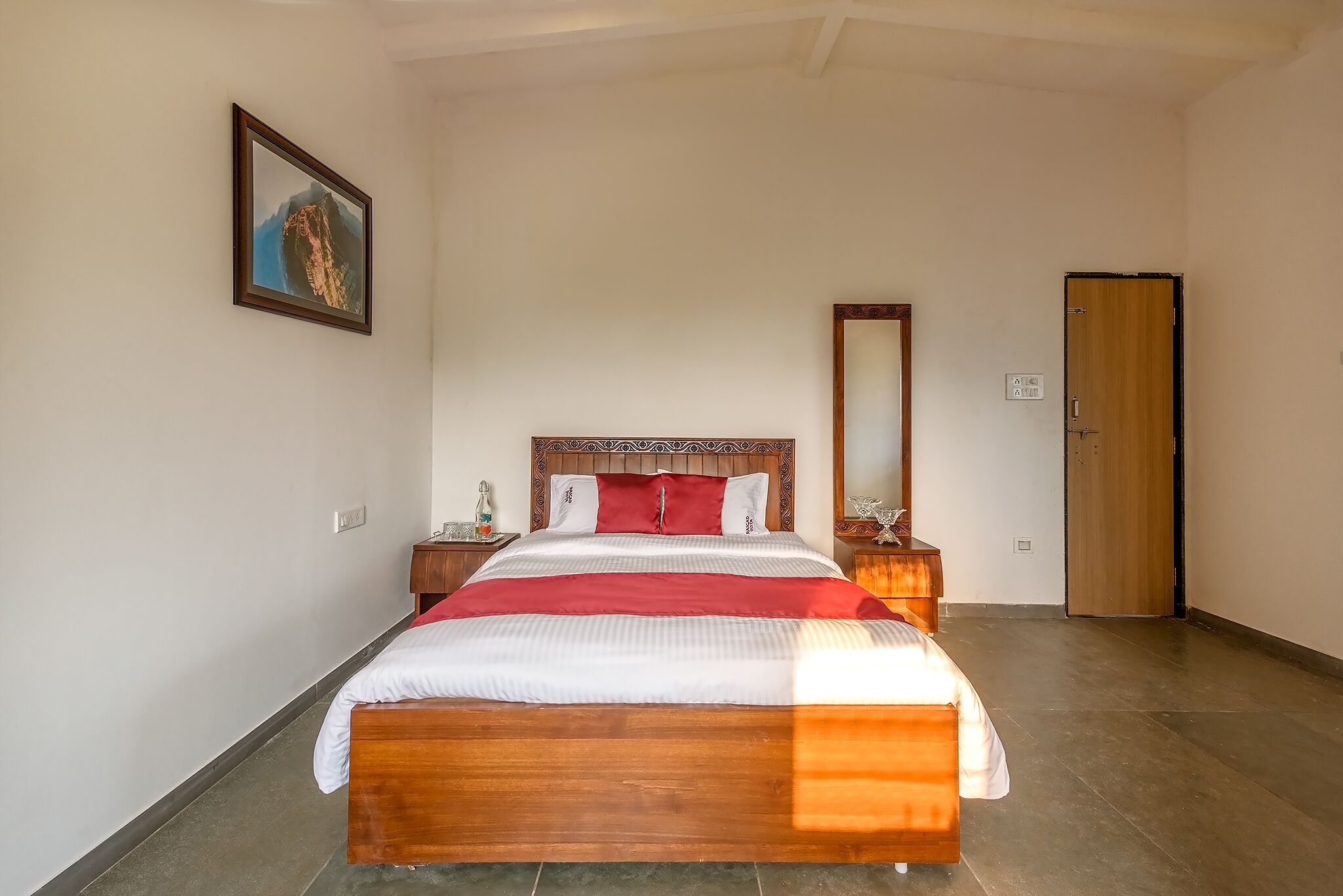 A neatly arranged bedroom with a wooden bed, a nightstand, a mirror, and a door.