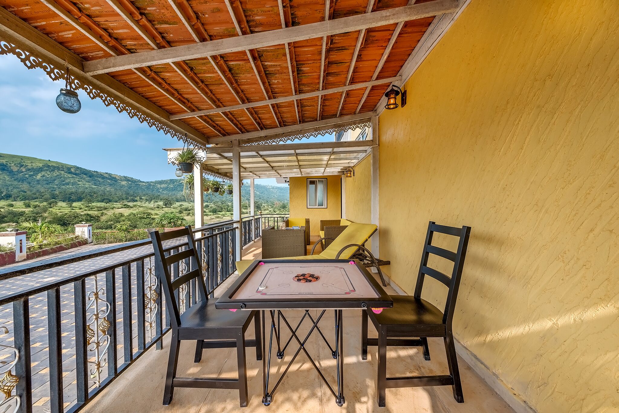 A balcony with a table and chairs, a view of the countryside, and a yellow wall.