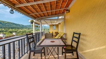 A balcony with a table and chairs, a view of the countryside, and a yellow wall.