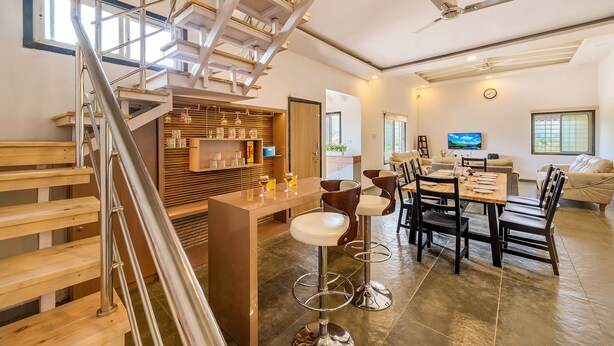 A modern kitchen with a central island, a dining area with bar stools, and a staircase with a metal railing.