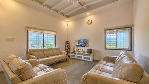 A spacious living room with two beige leather sofas, a white entertainment unit, and a ceiling fan.