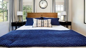A large bed with a blue patterned bedspread, two bedside tables with lamps, and a round mirror on the wall.