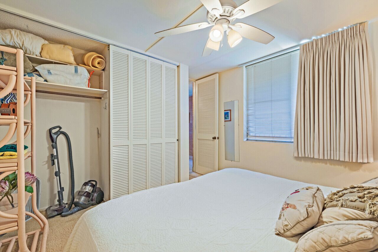 A bedroom with a bed, a ceiling fan, a closet, and a window with curtains.