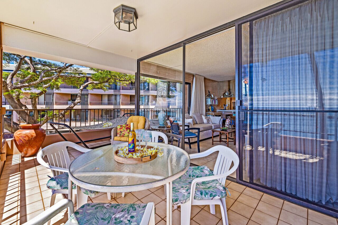 Ein Balkon mit Glastisch, weißen Stühlen und einem Blumentopf.