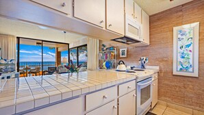 A modern kitchen with white cabinets, a large window offering a view of the sea, and a dining area with a view.