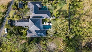 Vista aerea di una proprietà residenziale con piscina, diversi edifici e vegetazione tropicale circostante.
