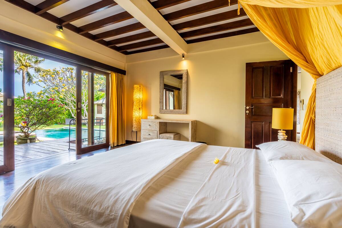 Ein Schlafzimmer mit einem großen Bett, einem Schreibtisch, einem Spiegel und Blick auf einen Pool.