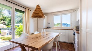 Eine moderne Küche mit Holztisch, weißen Stühlen, einer Pendelleuchte und Blick ins Grüne.