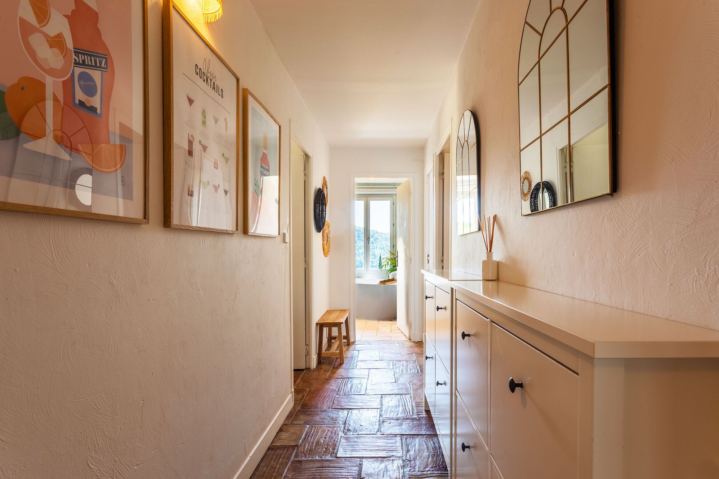 A hallway with framed artwork, a wooden bench, and a white cabinet with drawers.