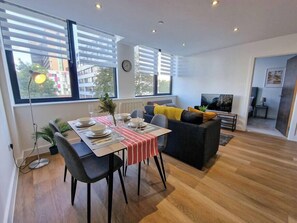 Uma sala de estar moderna com área de jantar, janelas amplas, sofá e televisão.
