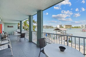 Un balcon avec des sièges d’extérieur, une vue sur l’eau et, au fond, un bâtiment portant l’inscription « Beach ».