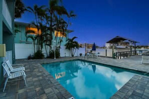 Une piscine avec des chaises longues, un espace de détente couvert et un bâtiment doté d’un balcon.