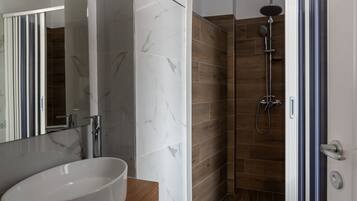 Un baño moderno con un lavabo de mármol, ducha con cabezal de ducha manual y tocador de madera.