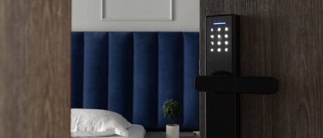 A modern bedroom with a bed, a nightstand, a small potted plant, and a wall-mounted electronic device.