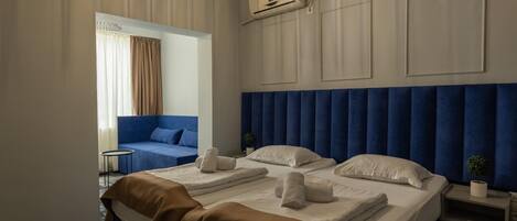 A hotel room with a large bed, a smaller sofa, a small table, and a potted plant.
