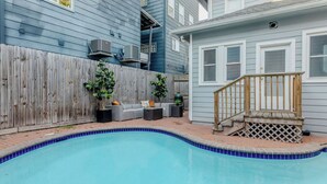 A backyard with a swimming pool, a wooden deck, a gray sofa set, and a wooden fence. - The Hera! Luxury Mansion in Montrose w/ Pool 4BR+1 (Houston)