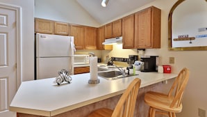 A modern kitchen with wooden cabinets, a white refrigerator, a sink, and a countertop with a kettle and a red container.