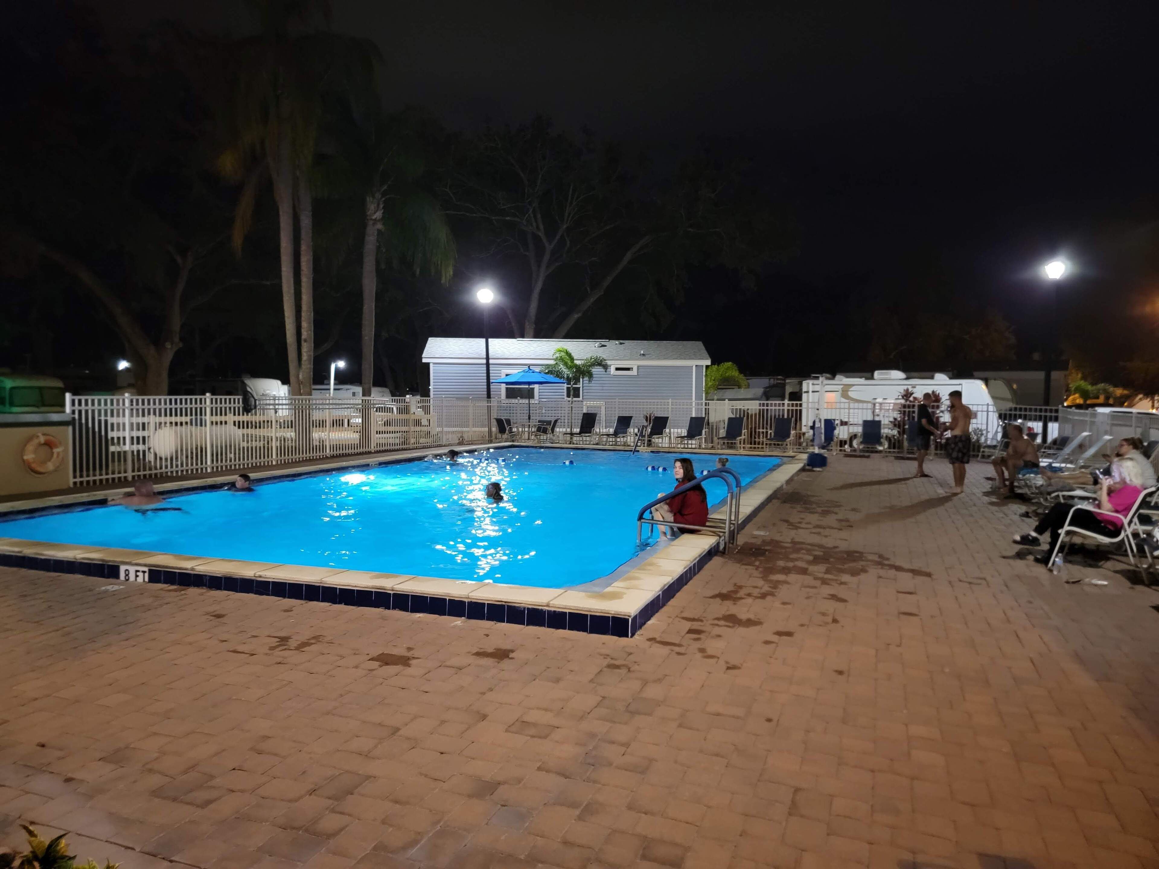 Una piscina con borde de azulejos, rodeada por una valla y un patio de ladrillo.