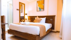 A neatly made bed with a wooden headboard, a large mirror, and a painting on the wall. - Kije Place Hotel (Nairobi)