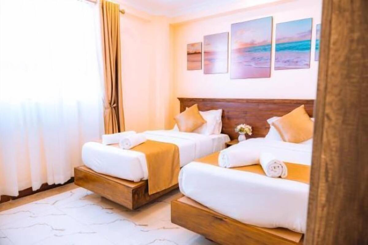 A hotel room with two beds, a wooden headboard, a white rug, and a view of the beach through the window.
