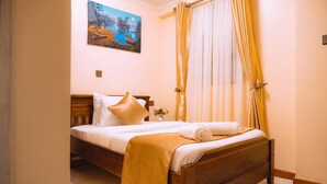 A neatly made bed with a wooden headboard, a bedside table with a vase of flowers, and a painting of a landscape on the wall. - Kije Place Hotel (Nairobi)