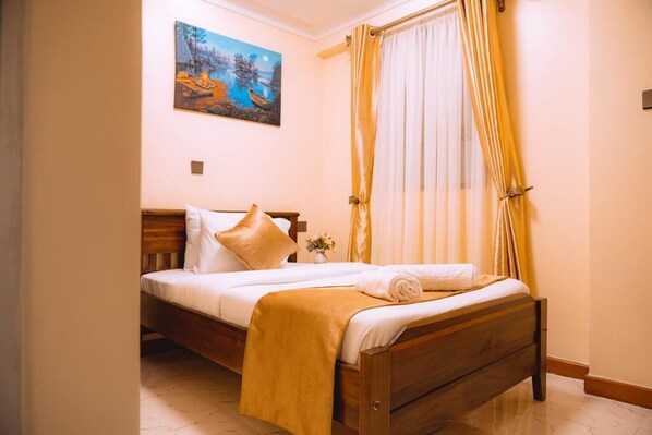 Una cama bien hecha con cabecera de madera, una mesita de noche con un florero y un cuadro de un paisaje en la pared.