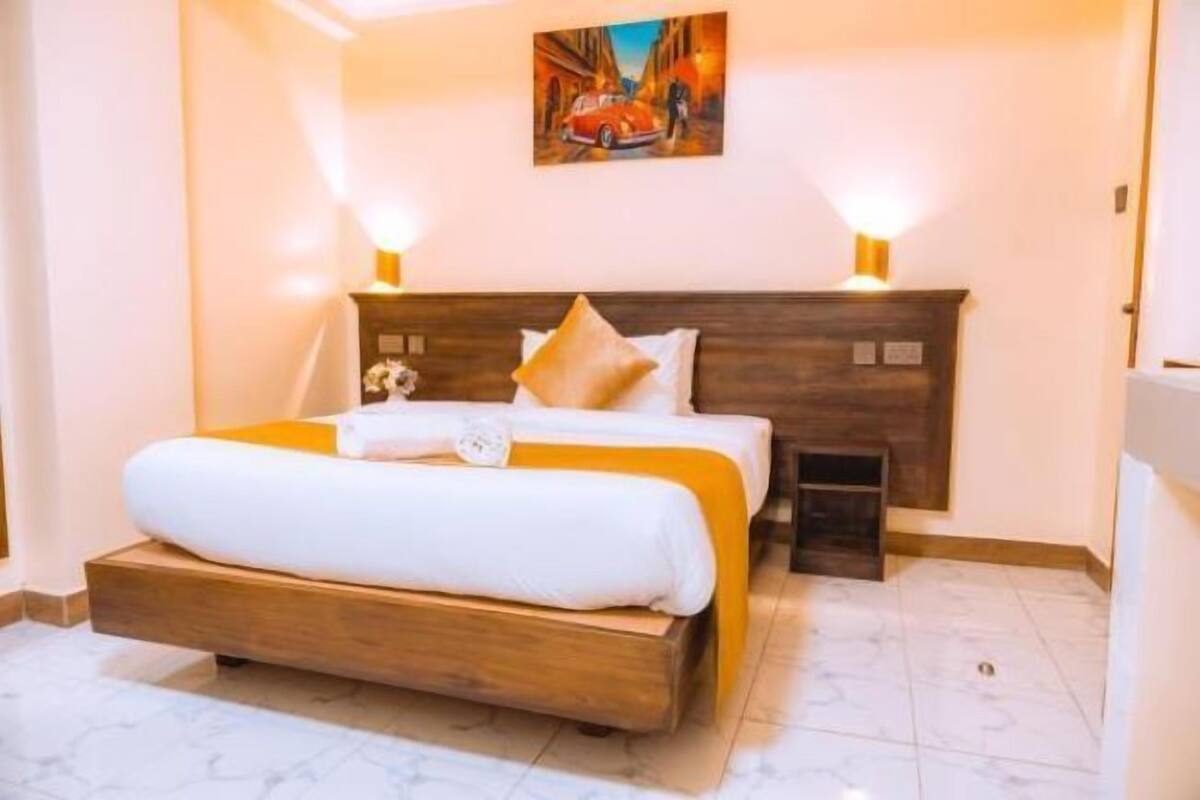 A bedroom with a wooden bed, white bedding, a nightstand, and a painting on the wall.