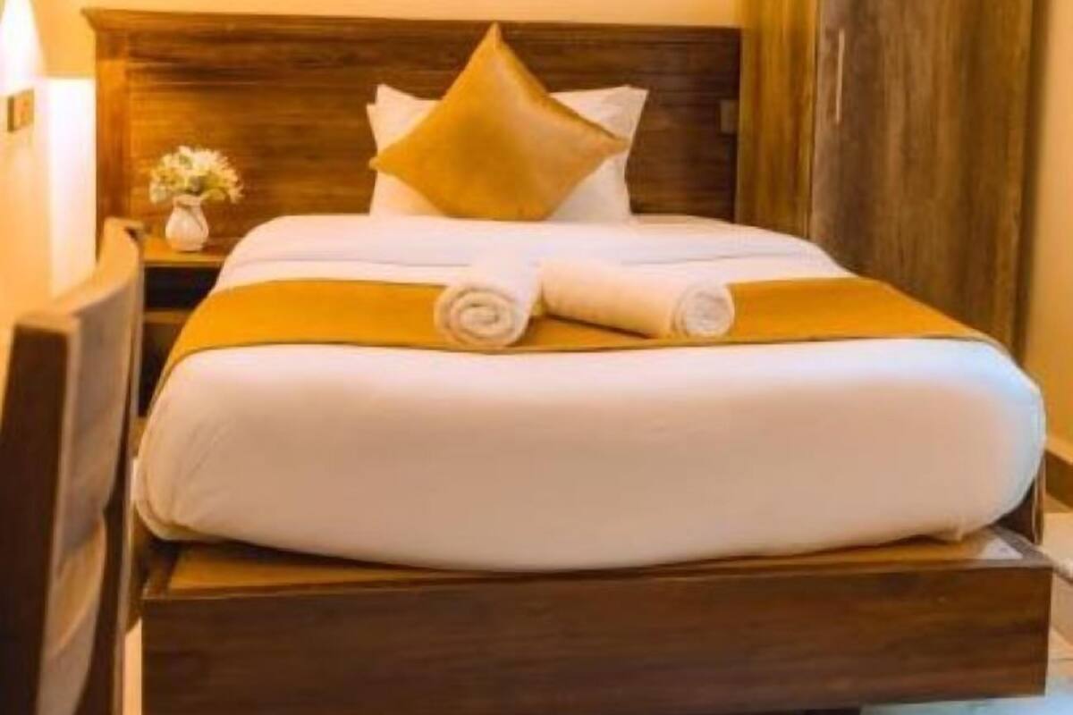 A neatly made bed with a wooden headboard, white bedding, and a rolled towel.