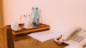 A wooden table with a tray holding a glass pitcher, two bottles of water, and a white cup. A telephone and remote control are also on the table. - Kije Place Hotel (Nairobi)