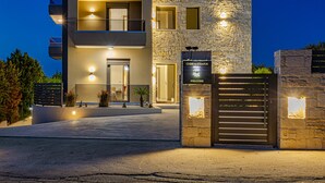 A modern two-story building with a stone facade, a welcoming sign, and a gated entrance. - Chris & Stratos villa with private pool and playground for kids! (Chania)