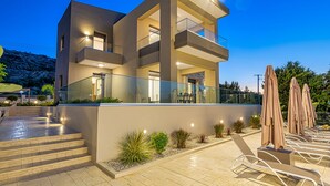 A modern multi-story building with a balcony, outdoor seating, and a well-lit entrance. - Chris & Stratos villa with private pool and playground for kids! (Chania)
