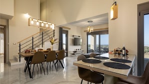 A modern dining area with a wooden table, black chairs, and a glass-top table. There is a staircase with a black railing leading to another level. - Chris & Stratos villa with private pool and playground for kids! (Chania)
