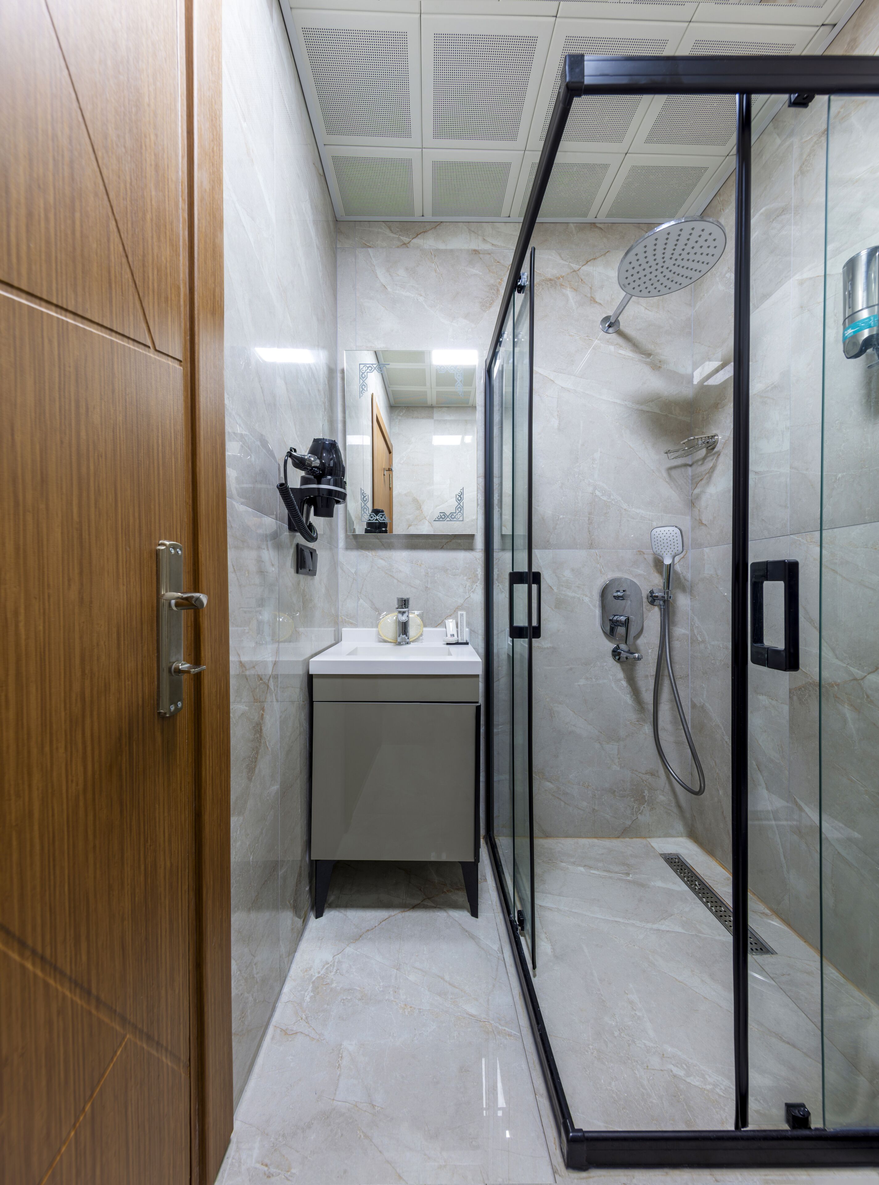 A modern bathroom with a wooden door, a marble sink, a glass shower enclosure, and a mirror.
