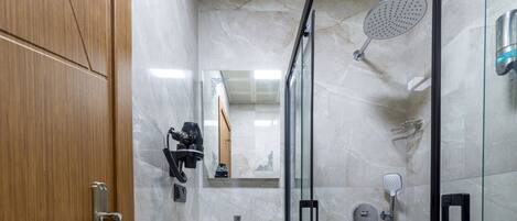 A modern bathroom with a wooden door, a marble sink, a glass shower enclosure, and a mirror.