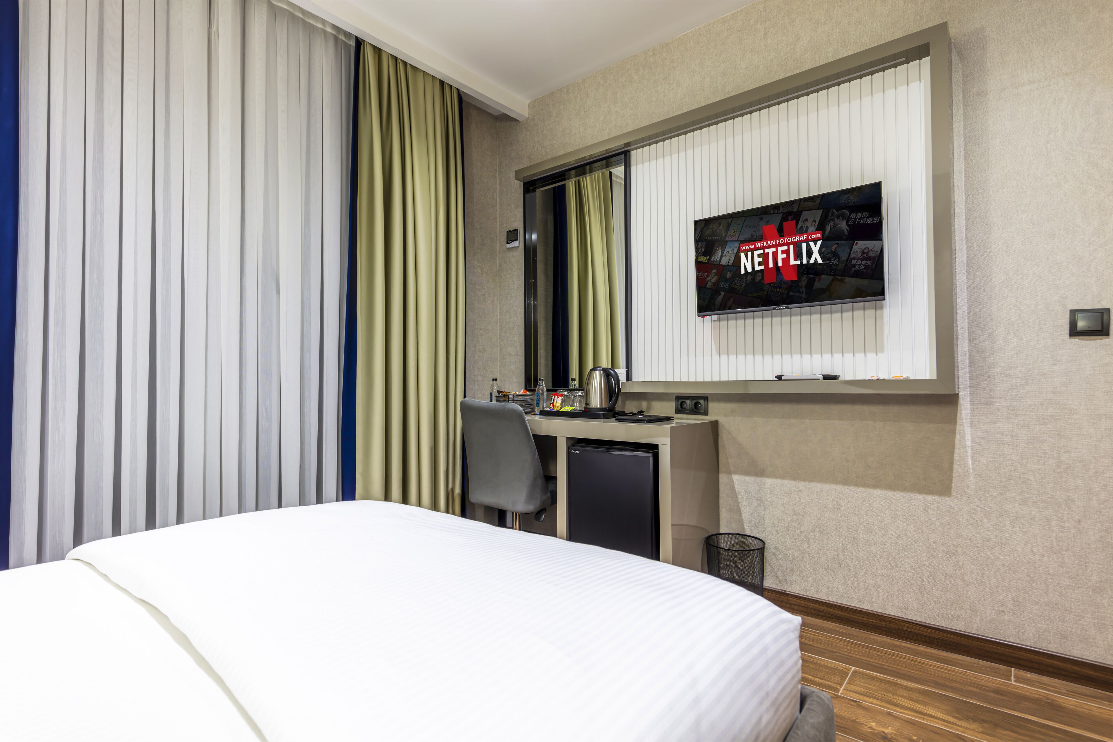 Hotelkamer met een bed, een bureau met een computer, een kleine kitchenette en een televisie aan de muur met het Netflix logo.