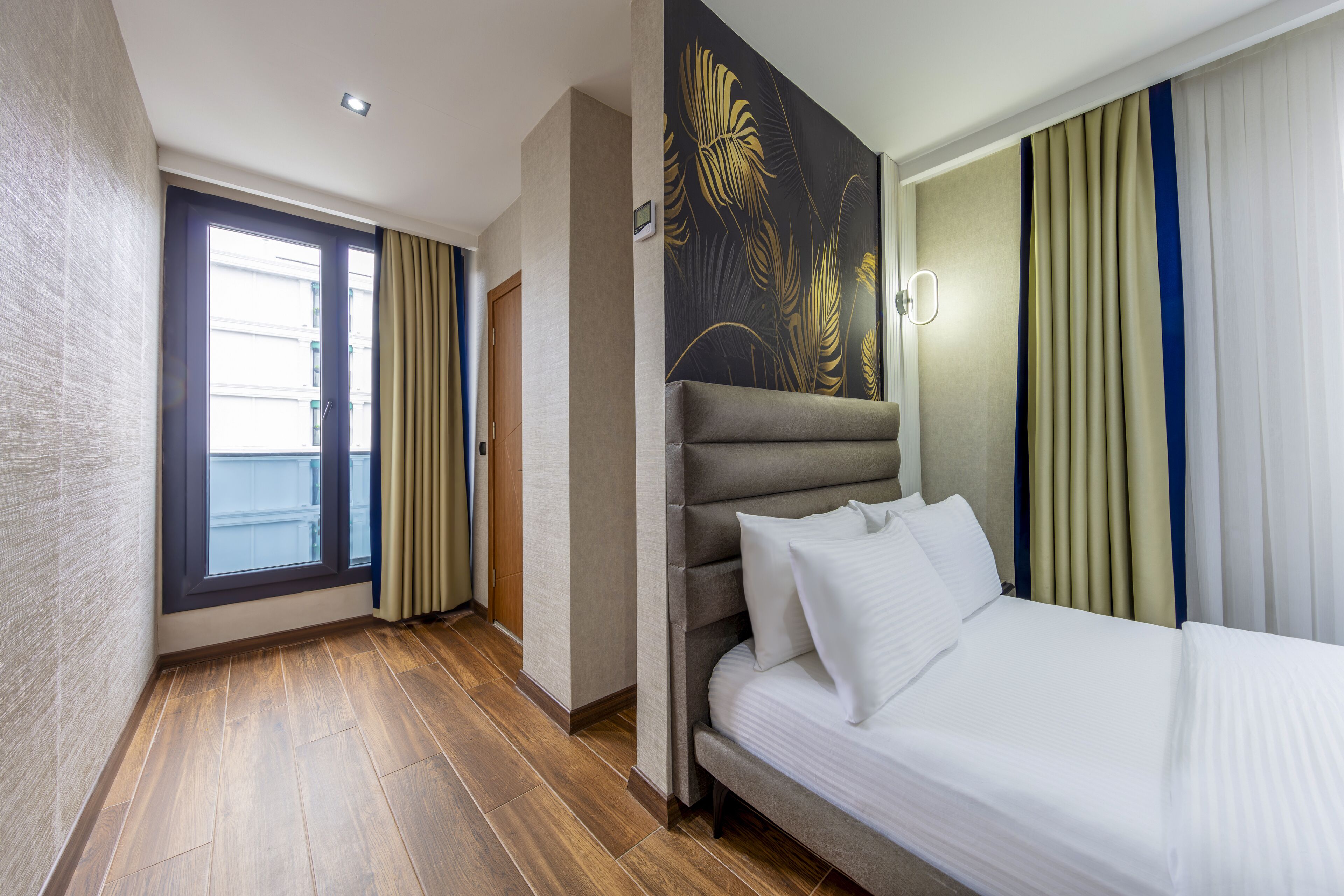 A hotel room with a large bed, a window with curtains, a door, and a wall with a floral pattern.