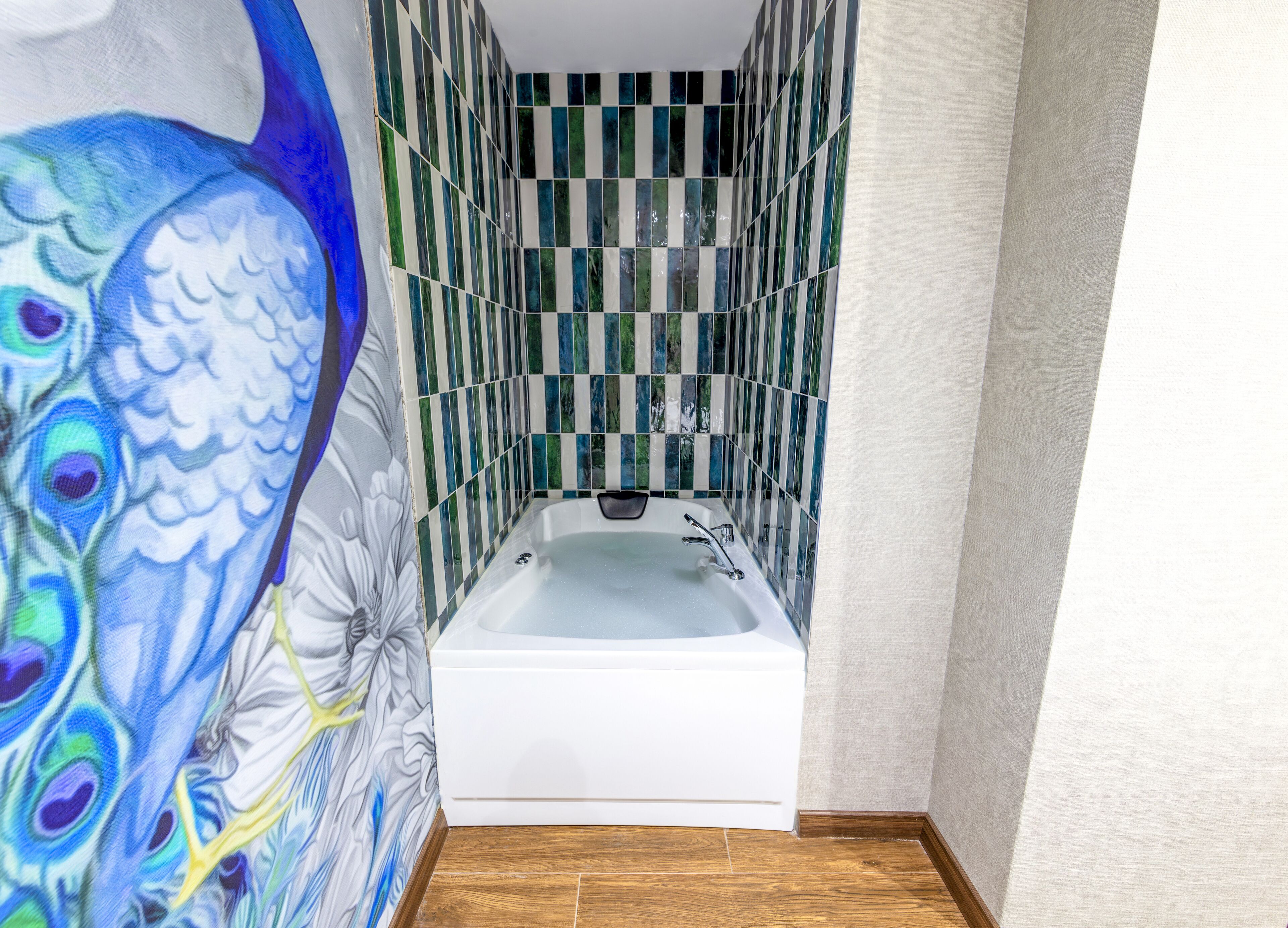 Ein Badezimmer mit einer weißen Badewanne, grün-weißen Streifenfliesen und einem Pfauenbild an der Wand.