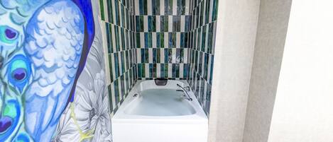A bathroom with a white bathtub, green and white striped tiles, and a peacock mural on the wall.