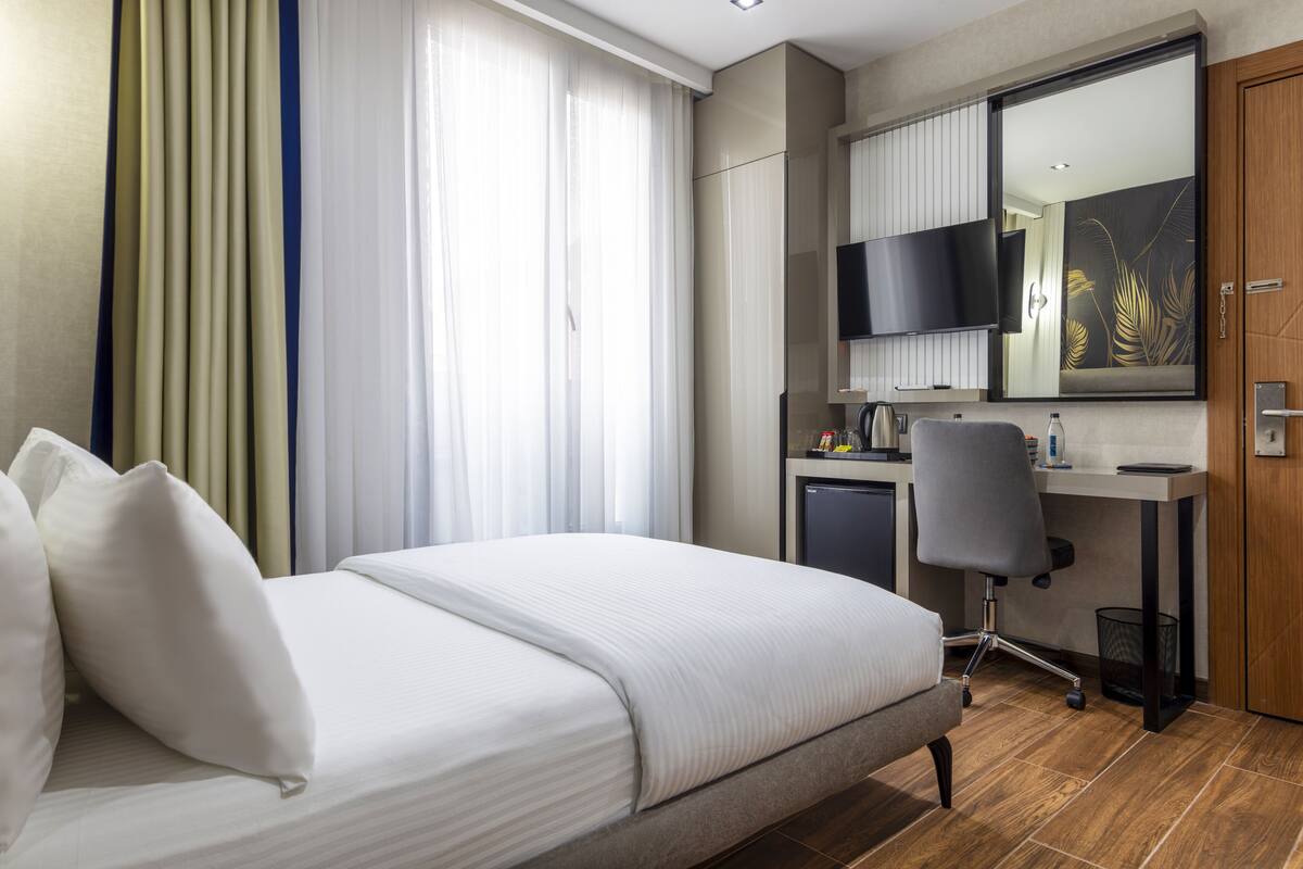 A hotel room with a bed, a desk with a chair, a television, and a mirror.