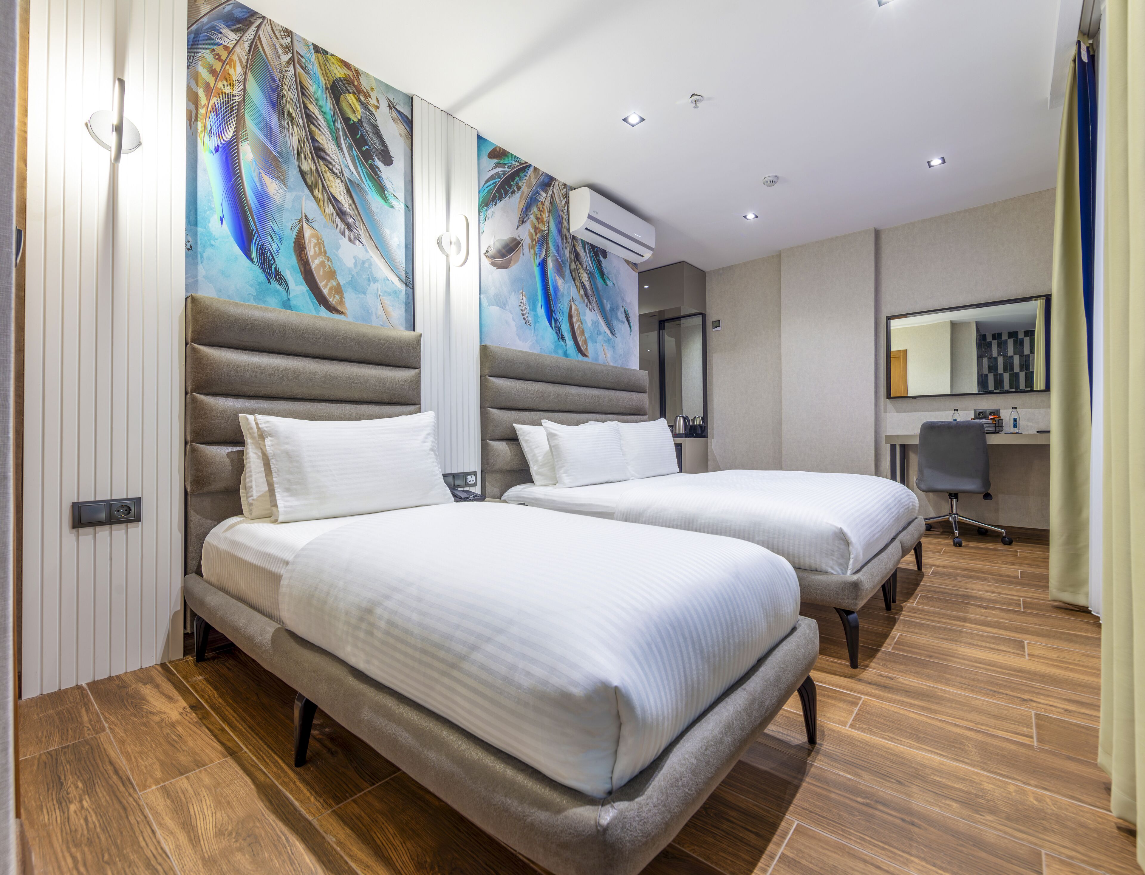 Habitación de hotel con dos camas, un cuadro grande en la pared, un equipo de aire acondicionado, un escritorio con una silla y un espejo.