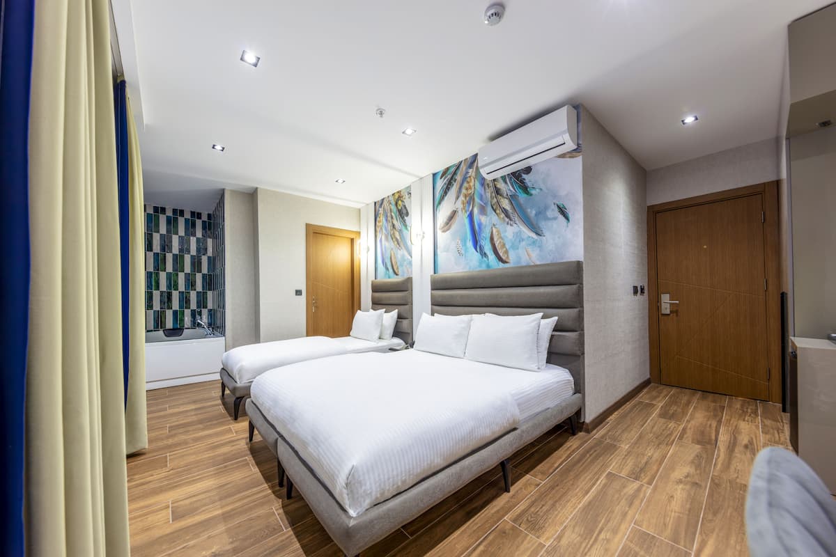 A hotel room with two beds, a wooden floor, an air conditioning unit, a painting on the wall, and a checkered wall decoration.