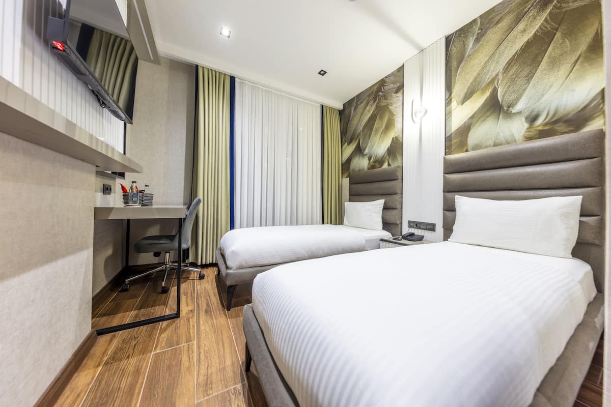 A hotel room with two beds, a desk, a chair, a TV, and a large wall mural.