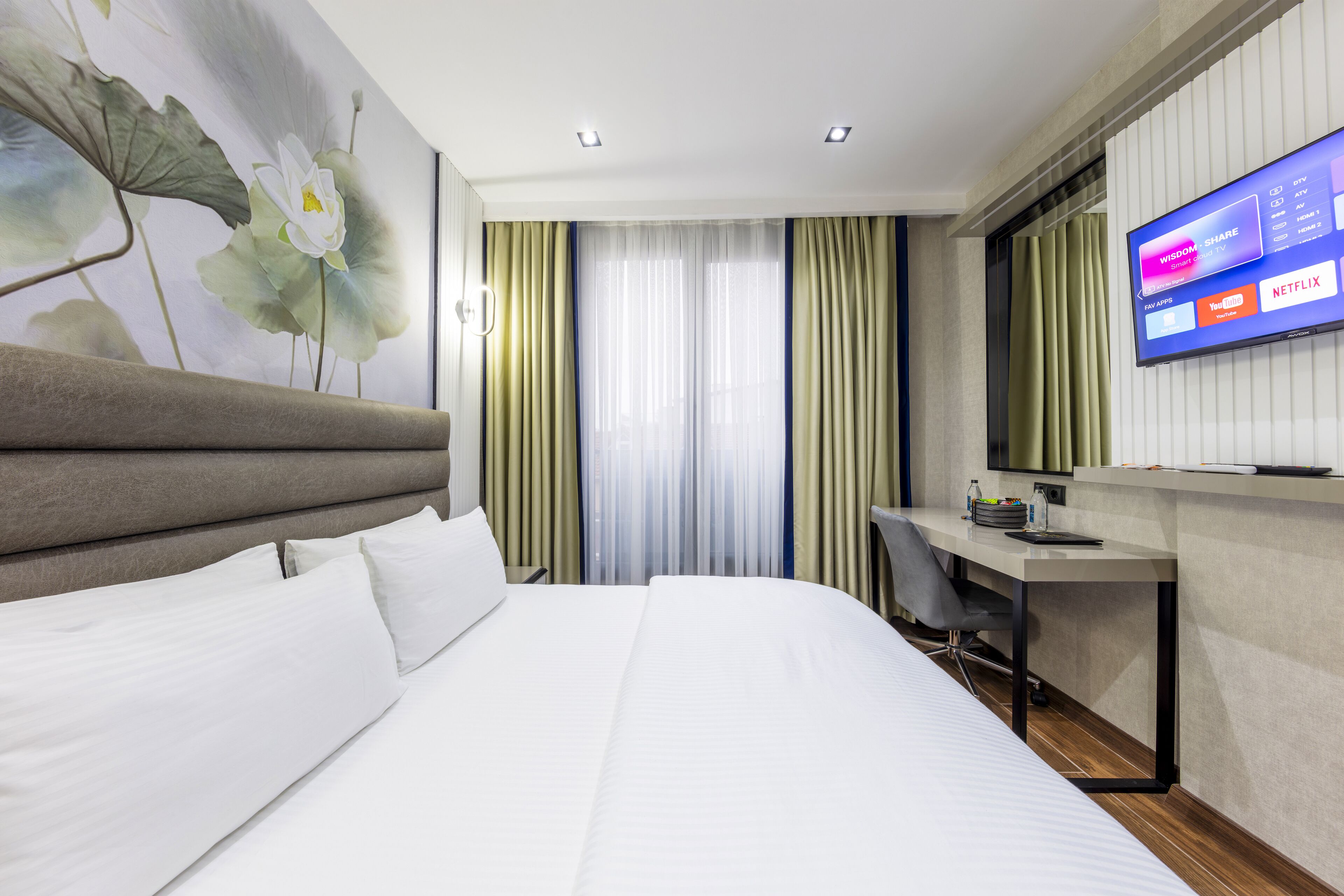 Une chambre d’hôtel équipée d’un lit, d’un bureau, d’un téléviseur permettant d’accéder à des services de diffusion en continu, et d’une grande œuvre d’art florale accrochée au mur.
